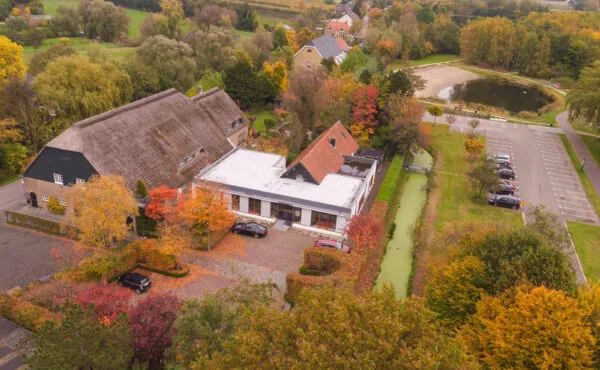 Luchtfoto van gebouwen aan de Charloisse Lagedijk in een herfstlandschap met parkeerplaats, vijver en omliggend groen.